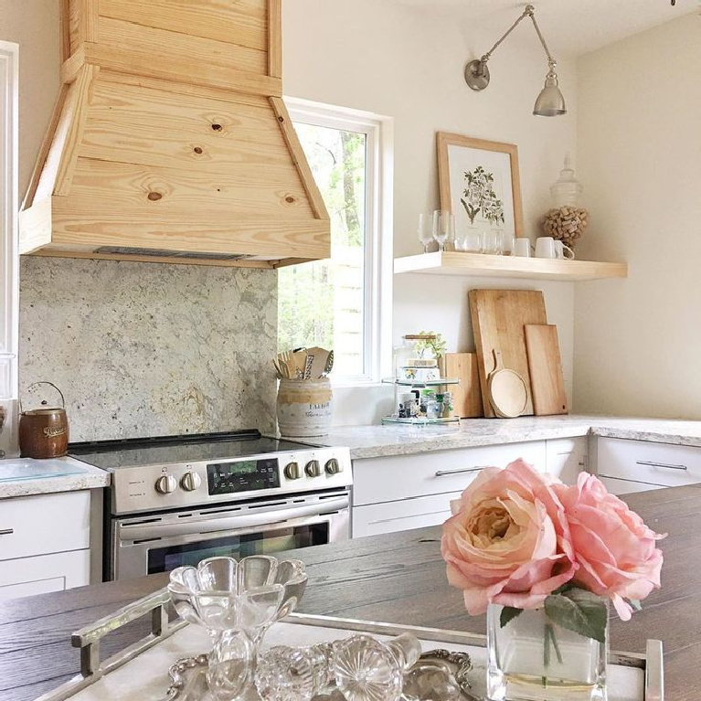 Rustic wood range hood in lovely white modern farmhouse kitchen with wood top on island - Lily Parker Home. #modernfarmhouse #kitchendesign #woodrangehood #farmhousekitchen