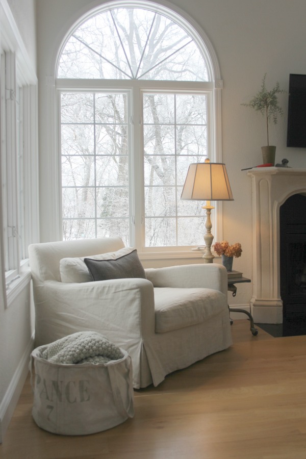 Belgian linen club chair in our living room with winter trees visible outside window. Hello Lovely Studio. Come visit 10 Smart Peaceful Ideas & Gifts to Give or Receive.