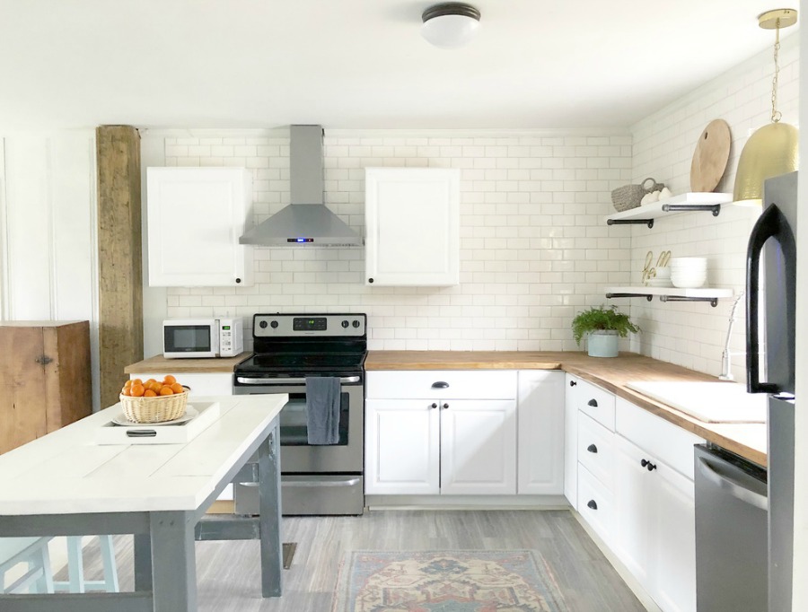 White cottage kitchen with subway tile, butcher block counters and stainless appliances.