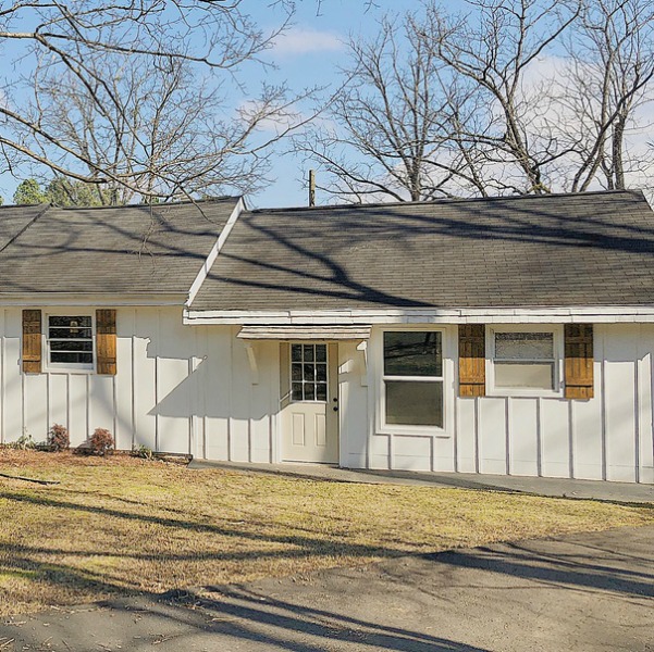 Charming white cottage with board and batten siding on exterior and rustic wood shutters flanking windows.