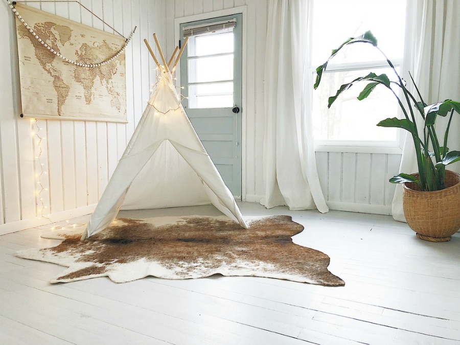 White teepee, fairy lights, and cowhide rug in white painted paneled modern farmhouse room.