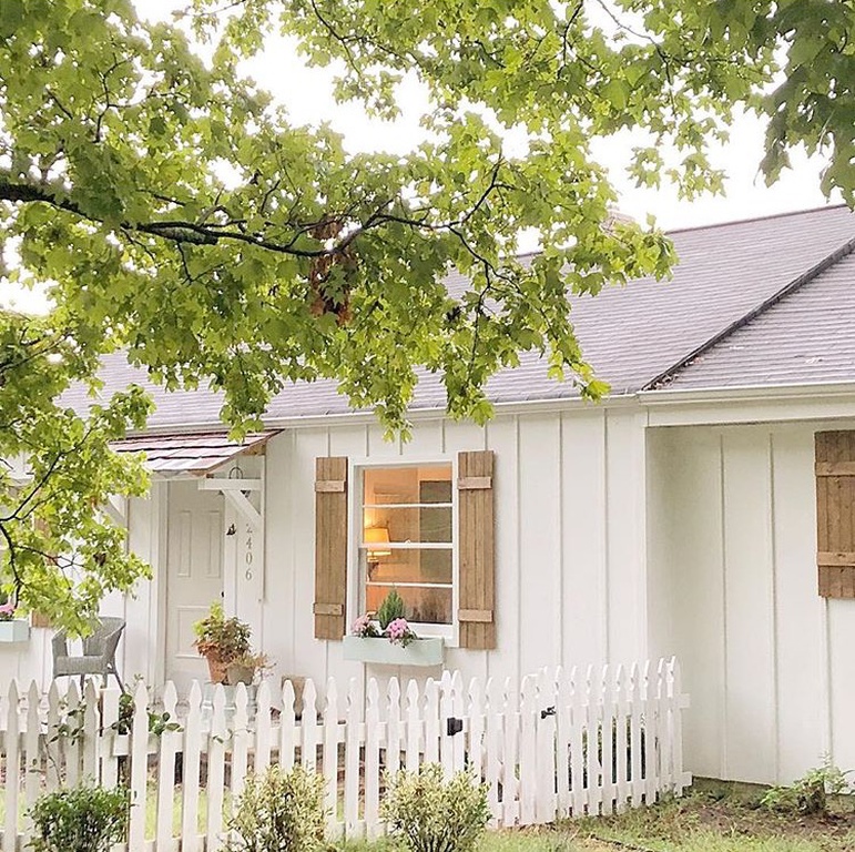 Charming white board and batten cottage exterior with rustic wood shutters.