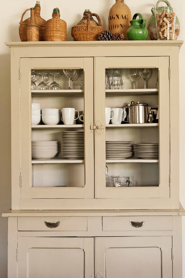 Tall grey painted cupboard stacked with rustic woven vintner's baskets in a French farmhouse kitchen. #frenchfarmhouse #kitchendesign #storage