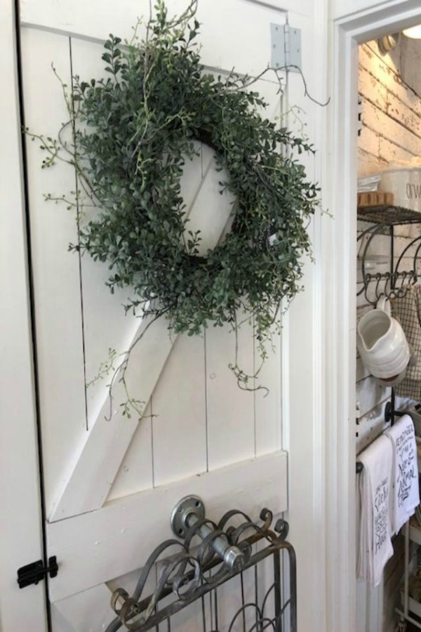 White barn door hung with wreath and garden gate wall decor at Urban Farmgirl. Photo by Hello Lovely Studio.