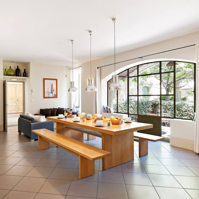 Modern style dining table and bench in a Provence villa dining area with large arched windows - Haven In.