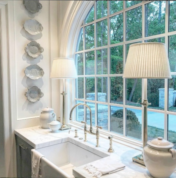 Timeless kitchen design with farm sink, arched window, marble counter, lamps and antique plates on wall. Design Galleria & Lauren DeLoach for 2017 Southeastern Designer Showhouse in Atlanta.