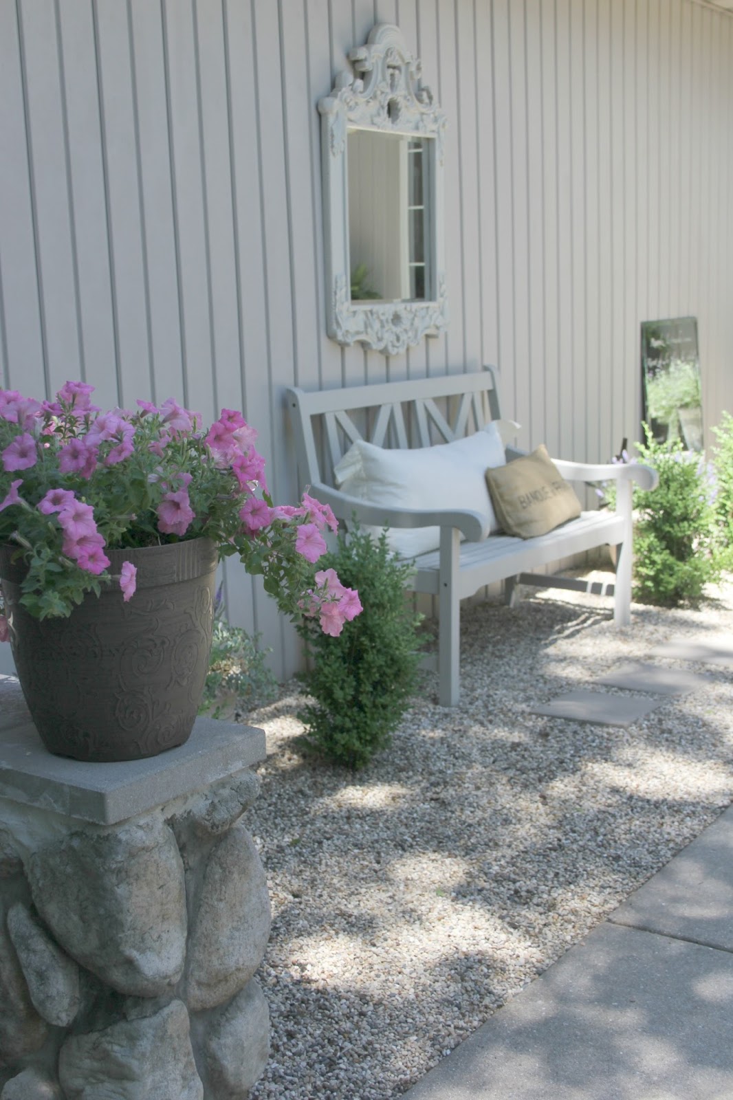 French courtyard with pink potted flowers, pea gravel, boxwood, and light grey bench - Hello Lovely Studio.