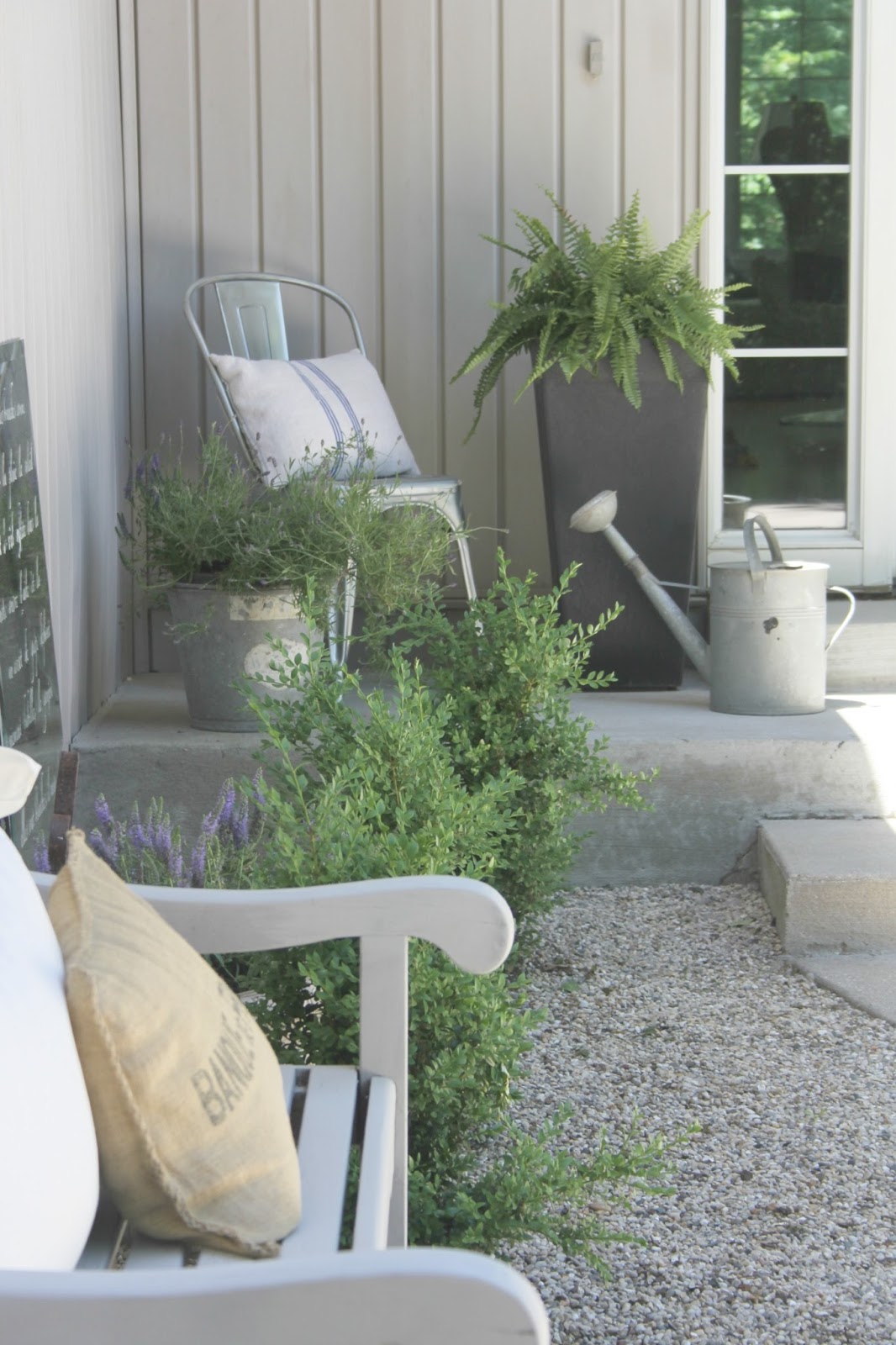 French farmhouse style courtyard with pea gravel, bench, boxwood, and galvanized farmhouse buckets - Hello Lovely Studio.