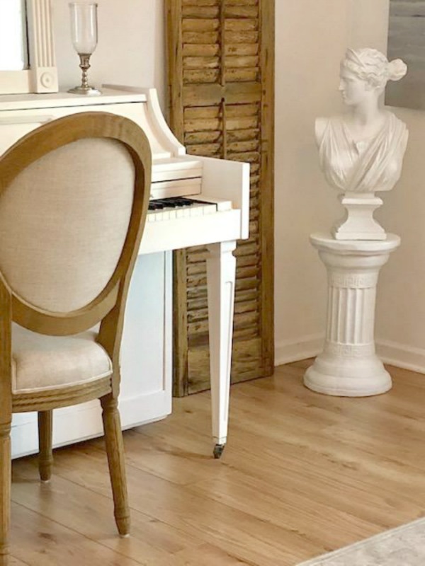 French farmhouse style and neutral palette in a studio with white piano, rustic shutter, and white bust of Diana. Piano is painted Benjamin Moore White Dove, and walls are Benjamin Moore White.