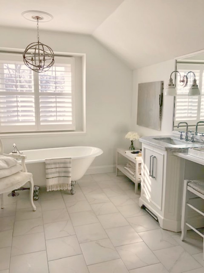 White cottage style bathroom with clawfoot tub, plantation shutters, and staggered calacatta tile floor - Hello Lovely Studio.