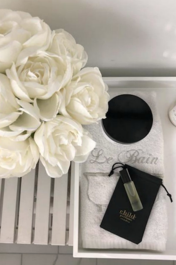 Black and white vignette with Child perfume and white roses in a bathroom by Hello Lovely Studio.