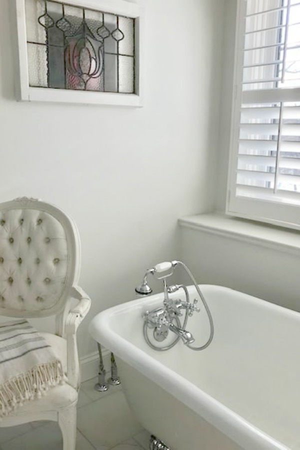 Romantic vintage style white bathroom with clawfoot tub and Louis French chair - Hello Lovely Studio.