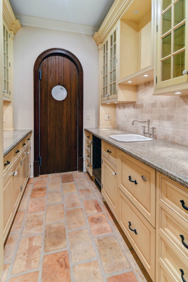 French farmhouse style in a scullery or pantry with rustic terracotta stone floor and painted cabinets in a grand Hinsdale home.