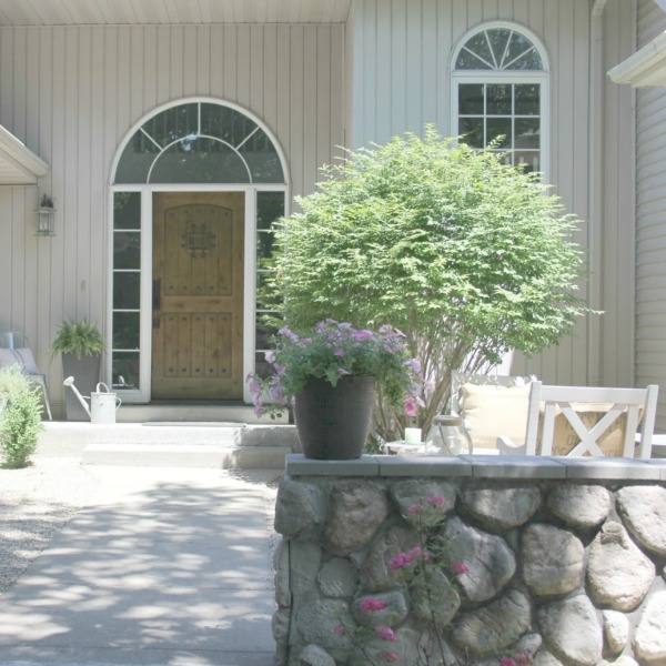 French farmhouse style courtyard with stone wall, rustic alder front door, and galvanized farmhouse decor - Hello Lovely Studio.