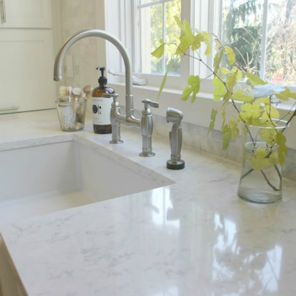 My white classic kitchen with Viatera quartz countertops in Minuet, Kohler Park bridge faucet, and farm sink. Hello Lovely Studio.