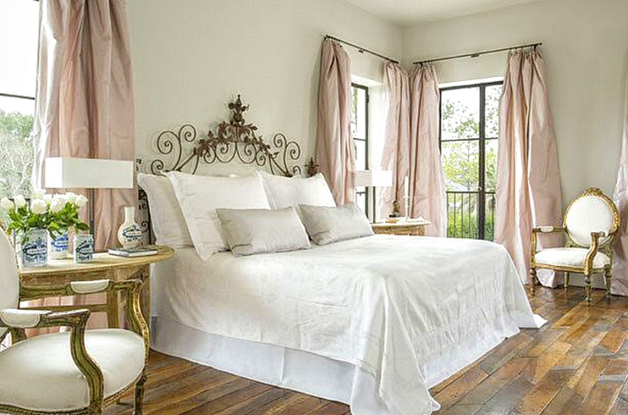 Elegant bedroom with French inspired decor, blush taffeta curtains, white bedding, and rustic wood floors. Come enjoy photos of this house tour with architecture by Reagan Andre.