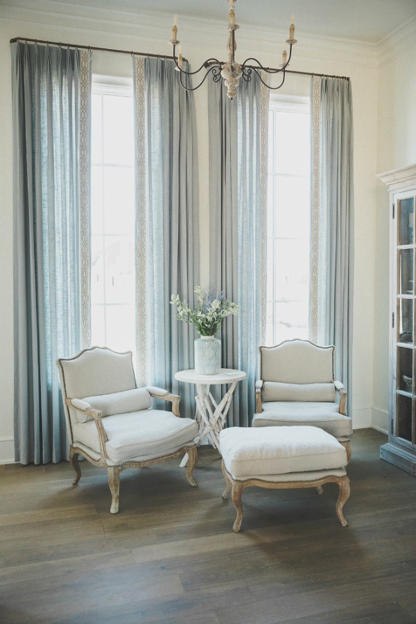 Classic French Bergere arm chairs and pale blue drapes in a French country room by Brit Jones with Sherwin Williams Alabaster paint.