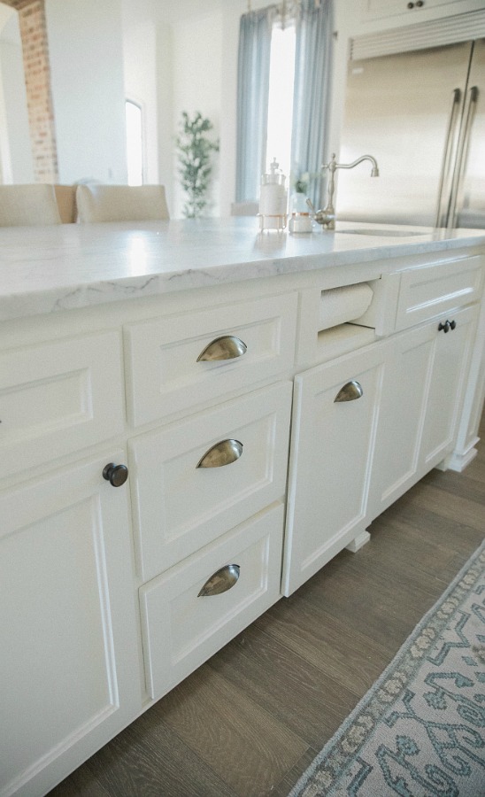 Detail of beautiful white Shaker style island topped with honed arabescato marble in French country kitchen with oak hardwood flooring. Brit Jones Design.