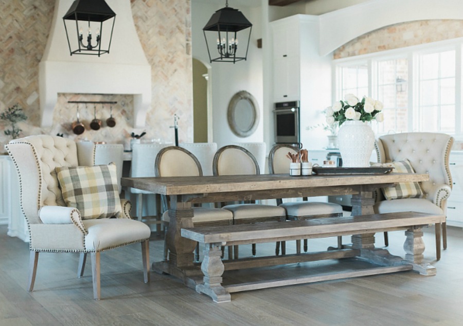 French country farmhouse kitchen with wingback chair, French dining chairs, farm table, rustic hanging lantern pendants, and reclaimed Chicago brick. Brit Jones Design.