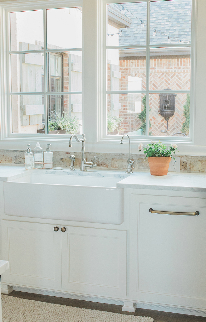 Rustic elegant French country farmhouse white kitchen with farm sink, reclaimed Chicago brick backsplash, and window overlooking courtyard. Brit Jones Design.