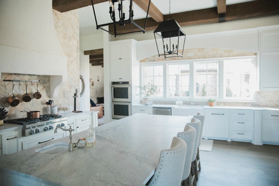 Elegant and rustic French country farmhouse white kitchen with rustic hanging lanterns over island, reclaimed Chicago brick, oak hardwood flooring, and farm sink. Brit Jones Design.