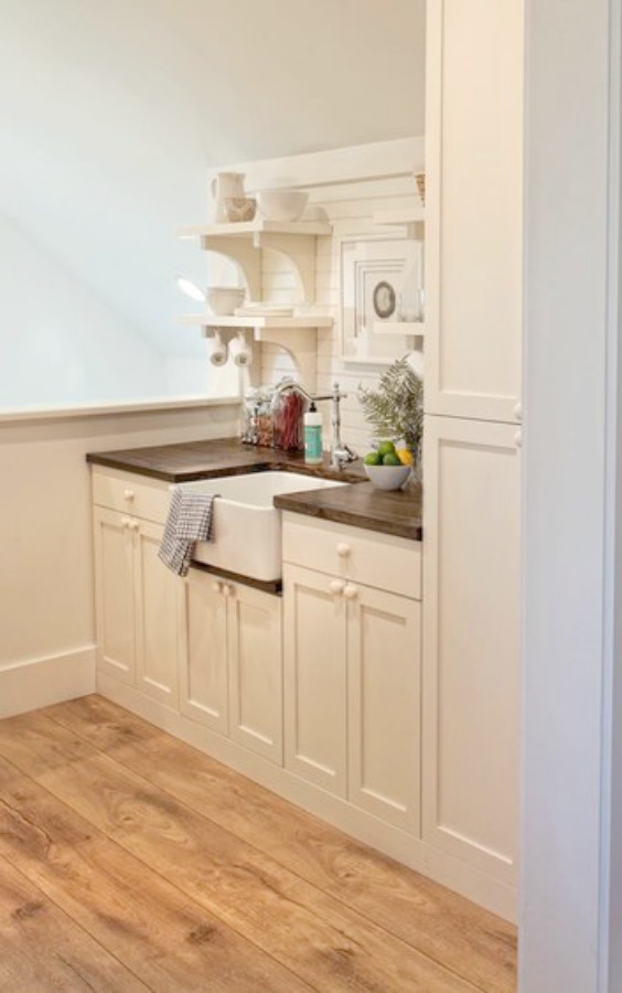 BM White OC-151. Coastal style kitchenette with custom Shaker cabinetry, farm sink, and open shelving in a charming carriage house by Lisa Furey.