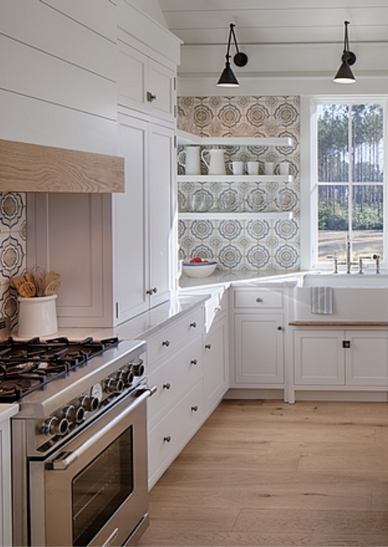 White coastal cottage kitchen with floating shelves, Shaker cabinets, white oak, and cement tile backsplash with blue accents. Lisa Furey. #coastalkitchen #whitekitchens #kitchendesign #modernfarmhouse #coastalcottage #cottagekitchen #floatingshelves #farmsink #shiplap