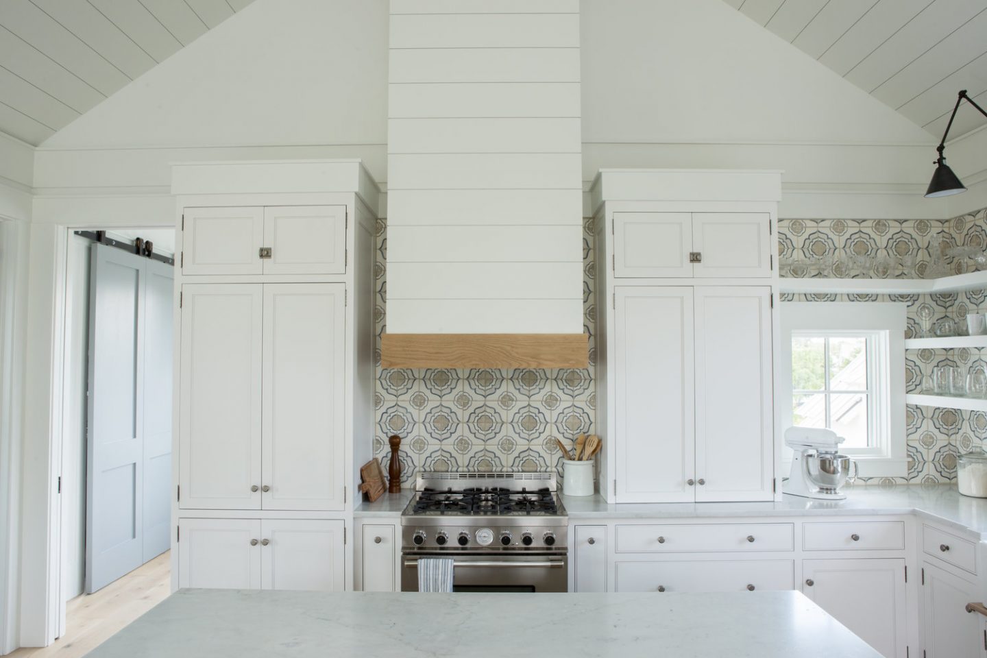 Classic white coastal cottage kitchen in Palmetto Bluff by Lisa Furey. Modern farmhouse design elements include floating shelves, shiplap, white oak flooring, and apron front farm sink.
