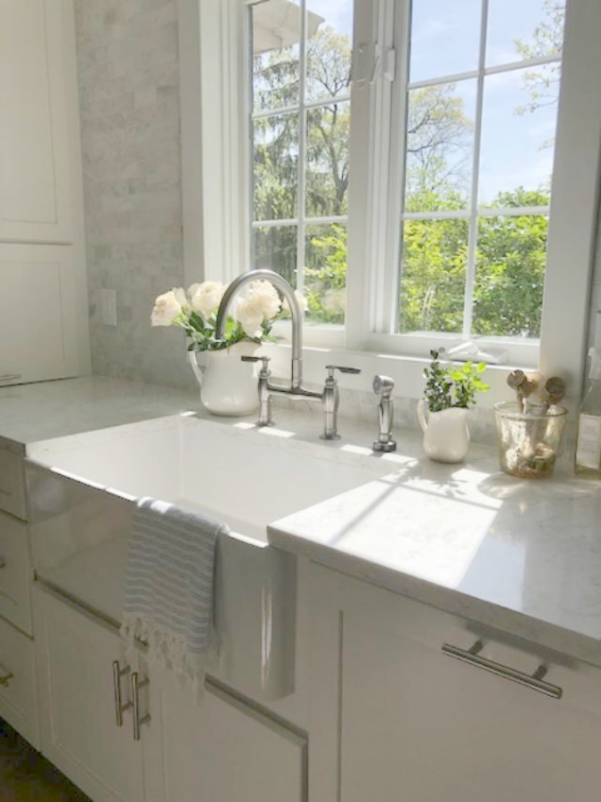 Serene tranquil white kitchen with farm sink, marble subway tile, Viatera Minuet quartz counters, white Shaker cabinets, and white oak flooring. Design and photo: Hello Lovely Studio. #kitchendesign #whitekitchen #minuet #whitequartz #benjaminmoorewhite