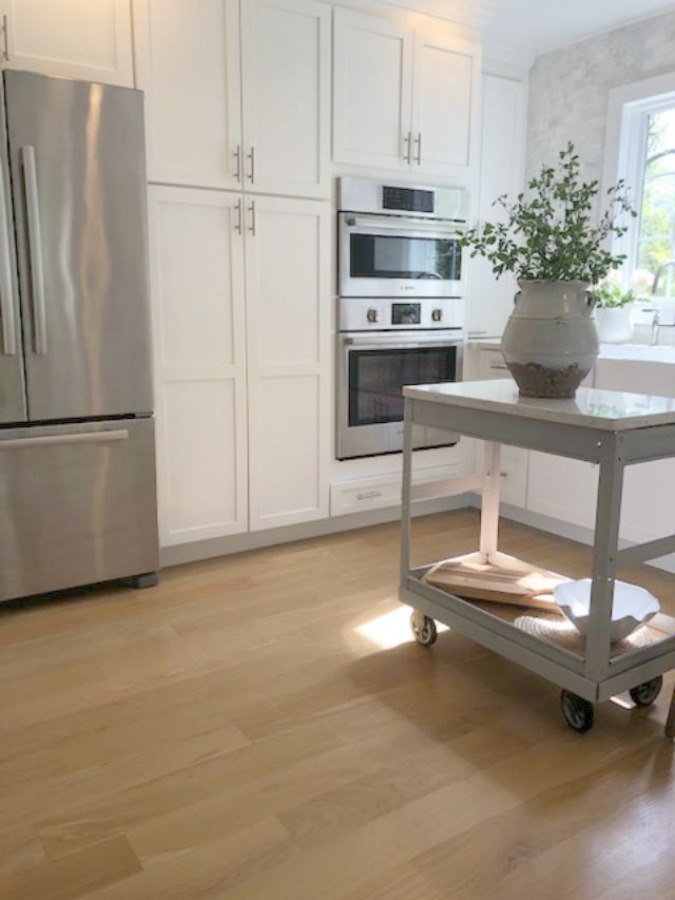 Serene tranquil white kitchen with farm sink, marble subway tile, Viatera Minuet quartz counters, white Shaker cabinets, and white oak flooring. Design and photo: Hello Lovely Studio. #kitchendesign #whitekitchen #minuet #whitequartz #benjaminmoorewhite