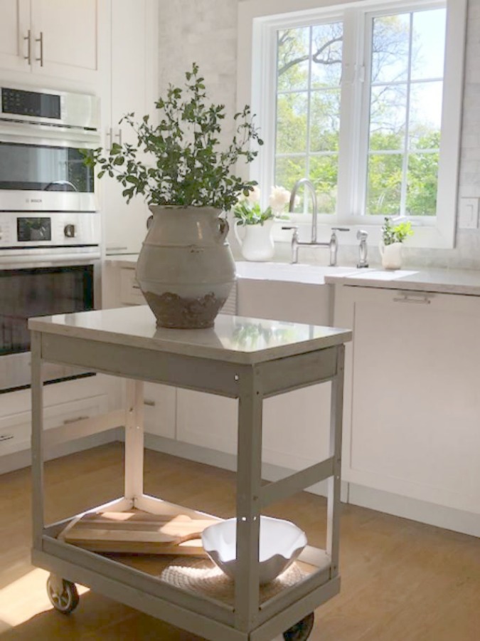 Serene tranquil white kitchen with farm sink, marble subway tile, Viatera Minuet quartz counters, white Shaker cabinets, and white oak flooring. Design and photo: Hello Lovely Studio. #kitchendesign #whitekitchen #minuet #whitequartz #benjaminmoorewhite