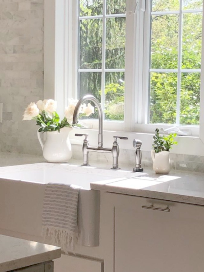 Serene tranquil white kitchen with farm sink, marble subway tile, Viatera Minuet quartz counters, white Shaker cabinets, and white oak flooring. Design and photo: Hello Lovely Studio. #kitchendesign #whitekitchen #minuet #whitequartz #benjaminmoorewhite