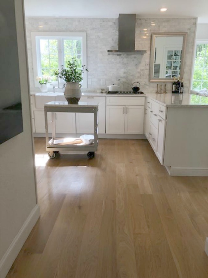 Serene tranquil white kitchen with farm sink, marble subway tile, Viatera Minuet quartz counters, white Shaker cabinets, and white oak flooring. Design and photo: Hello Lovely Studio. #kitchendesign #whitekitchen #minuet #whitequartz #benjaminmoorewhite