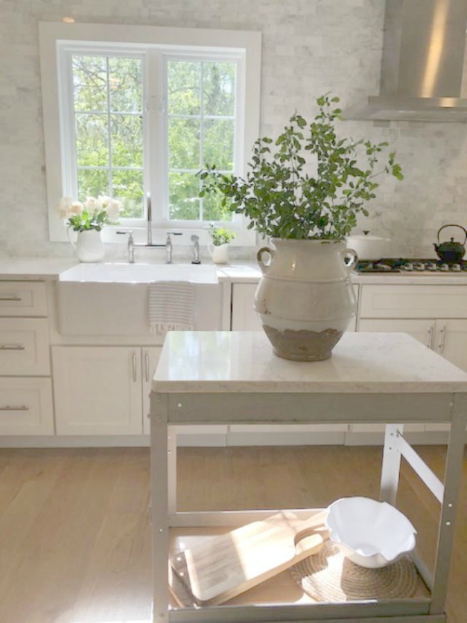 Serene tranquil white kitchen with farm sink, marble subway tile, Viatera Minuet quartz counters, white Shaker cabinets, and white oak flooring. Design and photo: Hello Lovely Studio. #kitchendesign #whitekitchen #minuet #whitequartz #benjaminmoorewhite