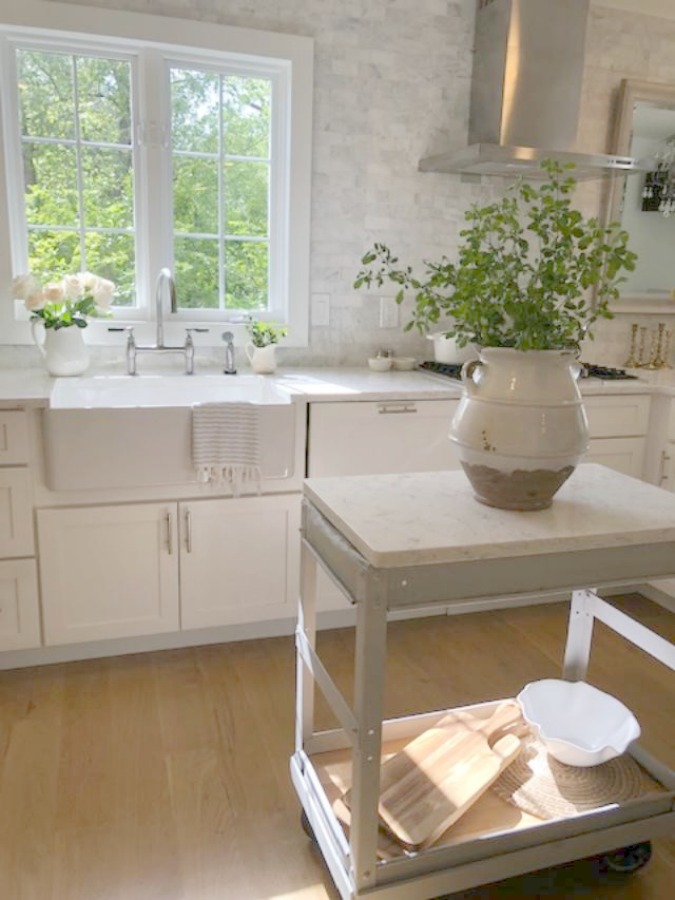 Serene tranquil white kitchen with farm sink, marble subway tile, Viatera Minuet quartz counters, white Shaker cabinets, and white oak flooring. Design and photo: Hello Lovely Studio. See more Gorgeous European Country Interior Design Inspiration on Hello Lovely. #europeancountry #frenchfarmhouse #interiordesign