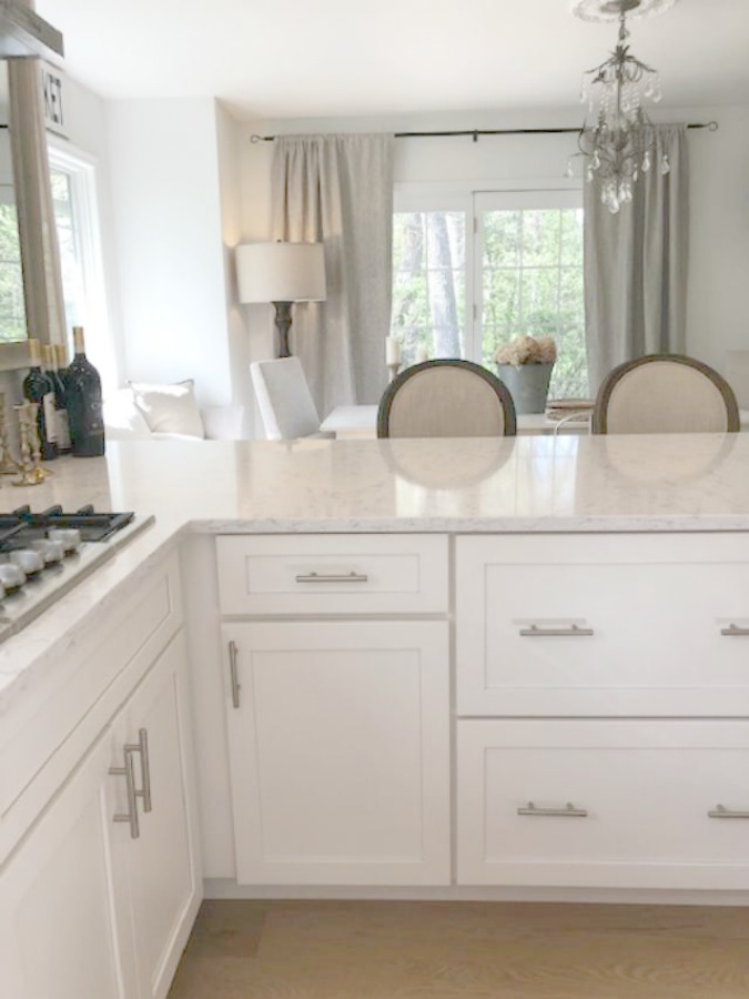 Serene tranquil white kitchen with farm sink, marble subway tile, Viatera Minuet quartz counters, white Shaker cabinets, and white oak flooring. Design and photo: Hello Lovely Studio. #kitchendesign #whitekitchen #minuet #whitequartz #benjaminmoorewhite