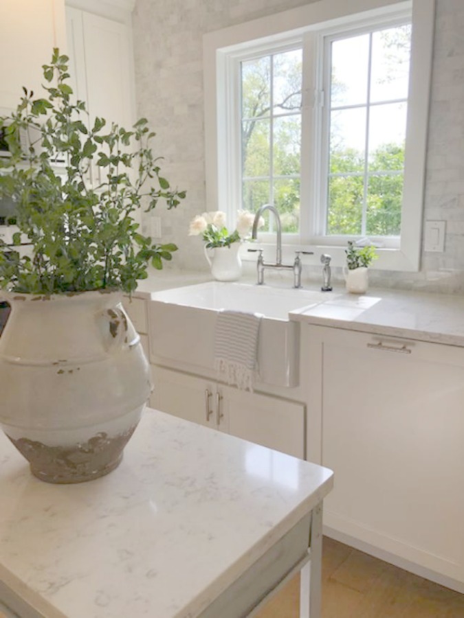 Serene tranquil white kitchen with farm sink, marble subway tile, Viatera Minuet quartz counters, white Shaker cabinets, and white oak flooring. Design and photo: Hello Lovely Studio. #kitchendesign #whitekitchen #minuet #whitequartz #benjaminmoorewhite