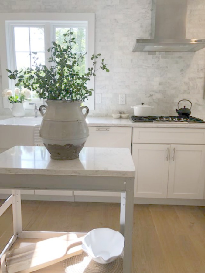 Serene tranquil white kitchen with farm sink, marble subway tile, Viatera Minuet quartz counters, white Shaker cabinets, and white oak flooring. Design and photo: Hello Lovely Studio. #kitchendesign #whitekitchen #minuet #whitequartz #benjaminmoorewhite