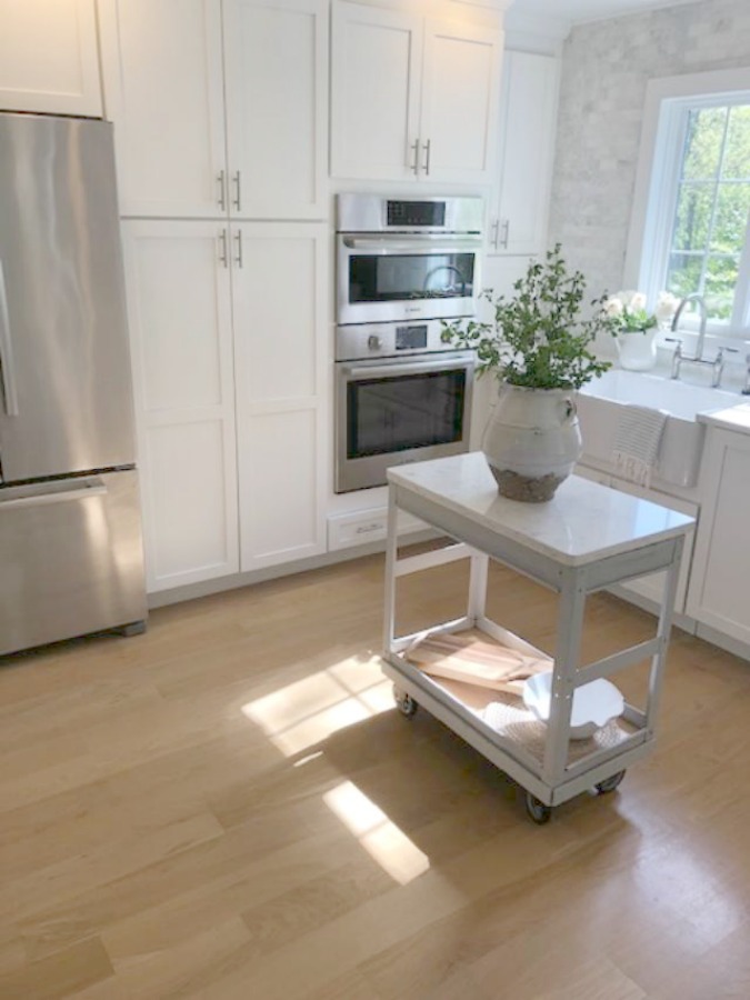 Serene tranquil white kitchen with farm sink, marble subway tile, Viatera Minuet quartz counters, white Shaker cabinets, and white oak flooring. Design and photo: Hello Lovely Studio. #kitchendesign #whitekitchen #minuet #whitequartz #benjaminmoorewhite