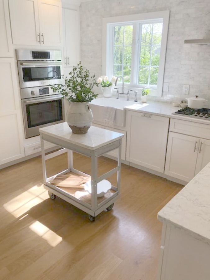 Serene tranquil white kitchen with farm sink, marble subway tile, Viatera Minuet quartz counters, white Shaker cabinets, and white oak flooring. Design and photo: Hello Lovely Studio. #kitchendesign #whitekitchen #minuet #whitequartz #benjaminmoorewhite