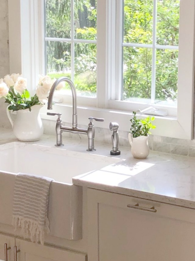 Serene tranquil white kitchen with farm sink, marble subway tile, Viatera Minuet quartz counters, white Shaker cabinets, and white oak flooring. Design and photo: Hello Lovely Studio. #kitchendesign #whitekitchen #minuet #whitequartz #benjaminmoorewhite