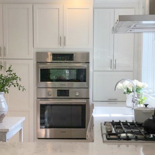 Serene tranquil white kitchen with farm sink, marble subway tile, Viatera Minuet quartz counters, white Shaker cabinets, and white oak flooring. Design and photo: Hello Lovely Studio. #kitchendesign #whitekitchen #minuet #whitequartz #benjaminmoorewhite