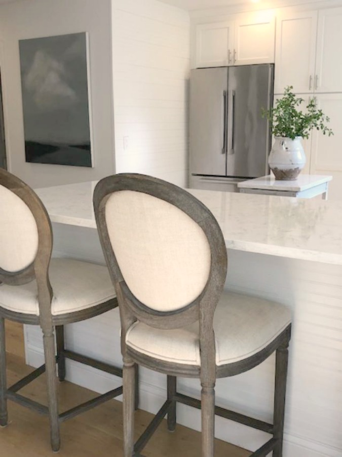 Serene tranquil white kitchen with farm sink, marble subway tile, Viatera Minuet quartz counters, white Shaker cabinets, and white oak flooring. Design and photo: Hello Lovely Studio. #kitchendesign #whitekitchen #minuet #whitequartz #benjaminmoorewhite