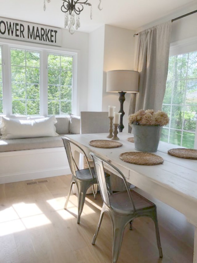 Serene tranquil white kitchen breakfast nook with farm table and window seat - Hello Lovely Studio. #whitecountrykitchen #whiteinteriors #countrykitchen #modernfrench