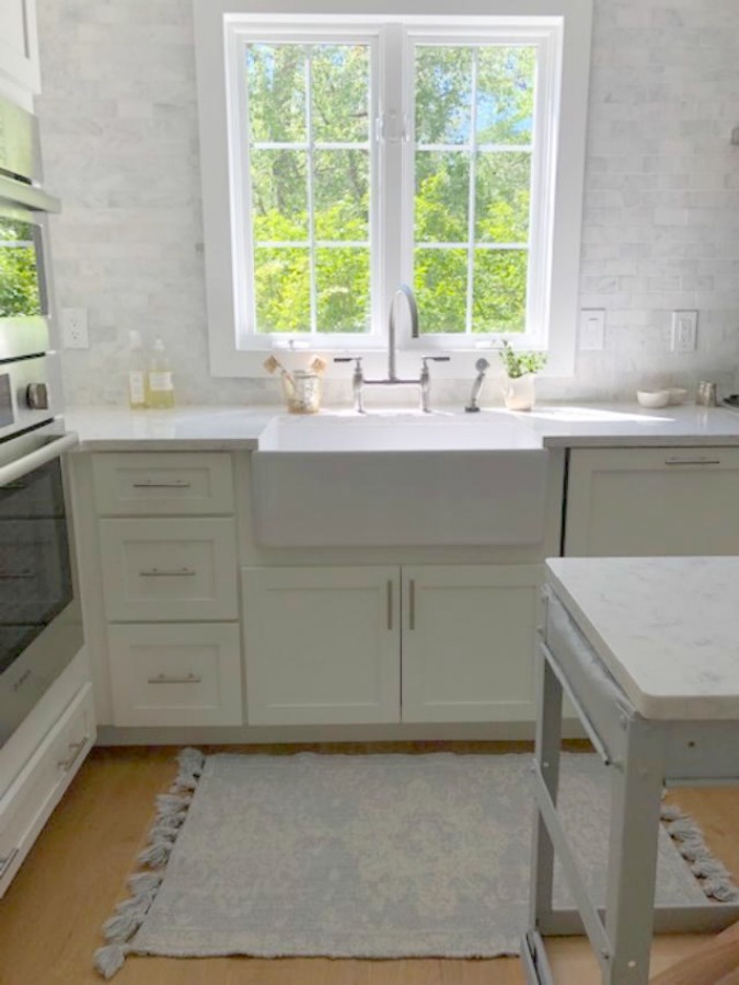 Serene tranquil white kitchen with farm sink, marble subway tile, Viatera Minuet quartz counters, white Shaker cabinets, and white oak flooring. Design and photo: Hello Lovely Studio. #kitchendesign #whitekitchen #minuet #whitequartz #benjaminmoorewhite