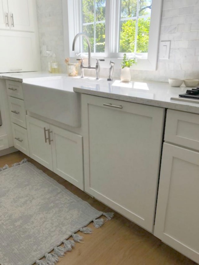 Serene tranquil white kitchen with farm sink, marble subway tile, Viatera Minuet quartz counters, white Shaker cabinets, and white oak flooring. Design and photo: Hello Lovely Studio. #kitchendesign #whitekitchen #minuet #whitequartz #benjaminmoorewhite