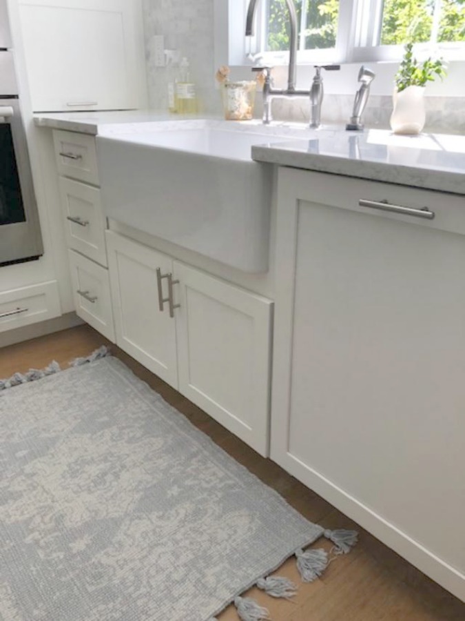 Serene tranquil white kitchen with farm sink, marble subway tile, Viatera Minuet quartz counters, white Shaker cabinets, and white oak flooring. Design and photo: Hello Lovely Studio. #kitchendesign #whitekitchen #minuet #whitequartz #benjaminmoorewhite