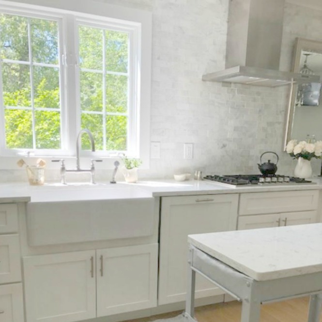 Serene tranquil white kitchen with farm sink, marble subway tile, Viatera Minuet quartz counters, white Shaker cabinets, and white oak flooring. Design and photo: Hello Lovely Studio. #kitchendesign #whitekitchen #minuet #whitequartz #benjaminmoorewhite