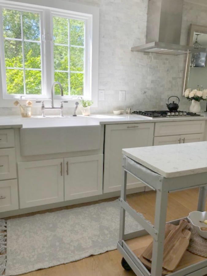 Serene tranquil white kitchen with farm sink, marble subway tile, Viatera Minuet quartz counters, white Shaker cabinets, and white oak flooring. Design and photo: Hello Lovely Studio. #kitchendesign #whitekitchen #minuet #whitequartz #benjaminmoorewhite