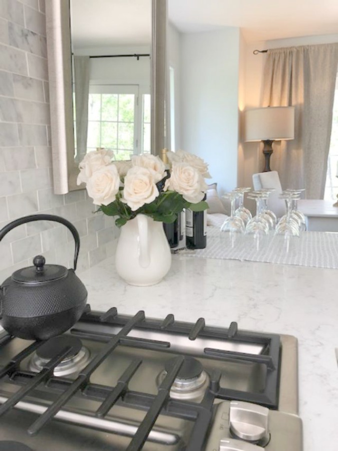 Serene tranquil white kitchen with farm sink, marble subway tile, Viatera Minuet quartz counters, white Shaker cabinets, and white oak flooring. Design and photo: Hello Lovely Studio. #kitchendesign #whitekitchen #minuet #whitequartz #benjaminmoorewhite